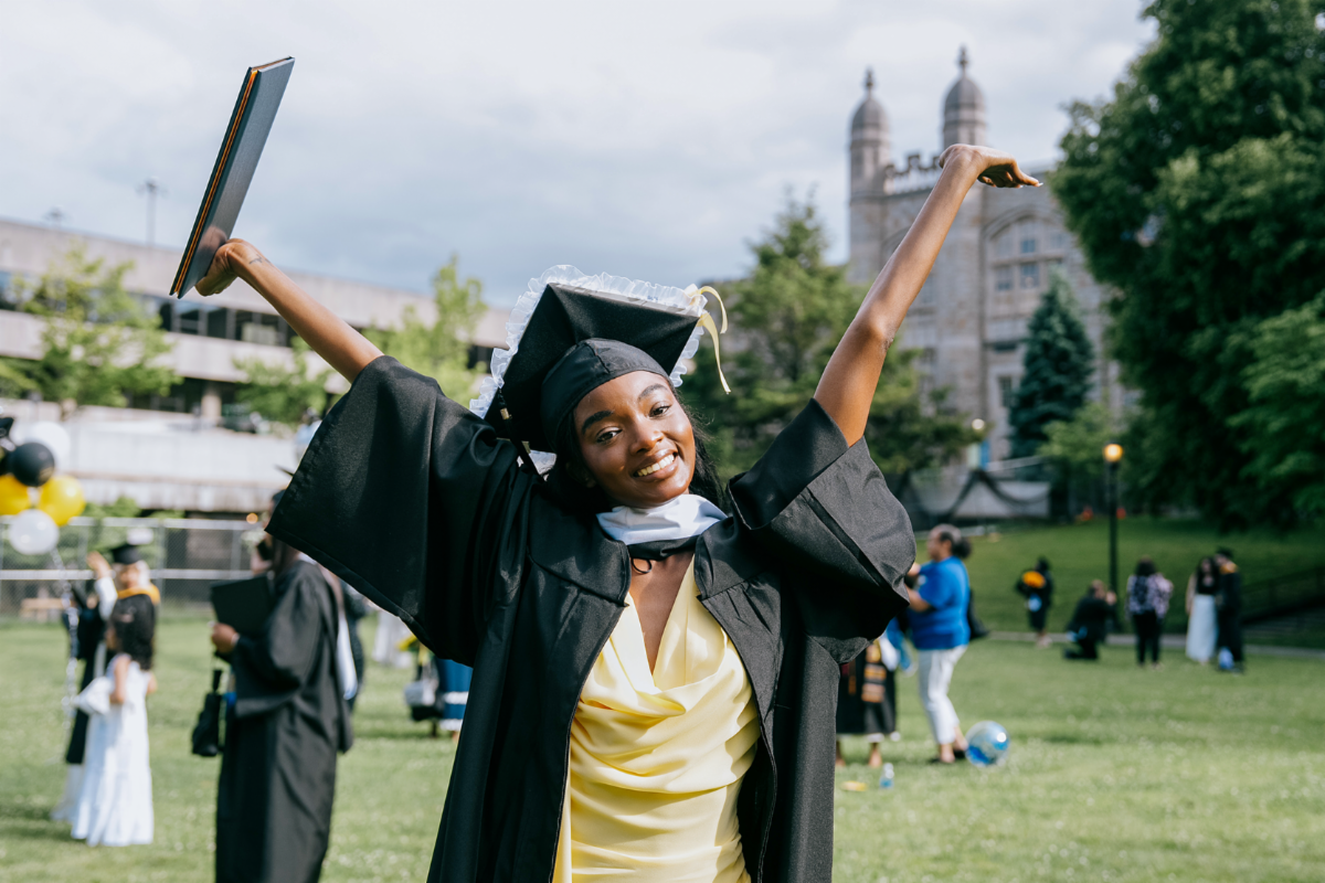 Graduate with arms outstretched in the air with diploma