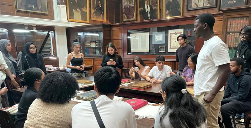 Students around table with oil portraits on wall around them 
