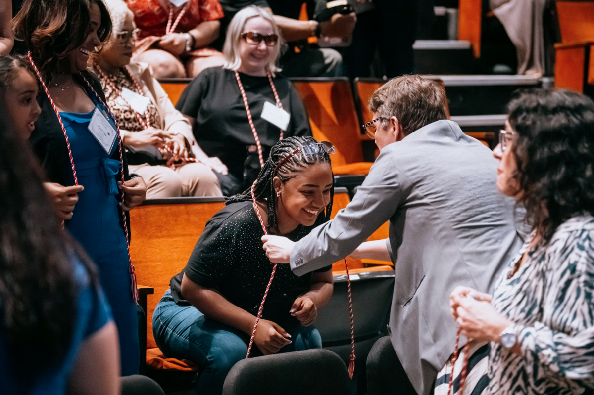 Professor placing an honor cord around a graduate’s neck.