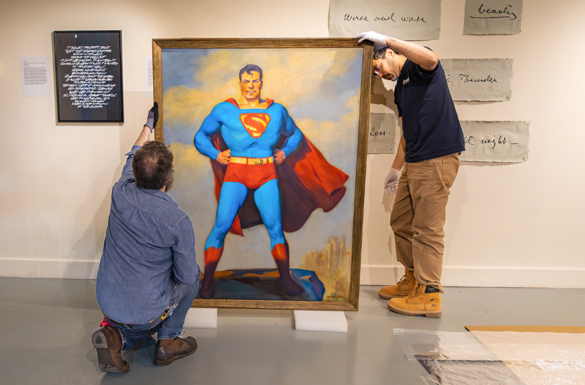 Two men installing a painting of Superman in Lehman's Art Gallery