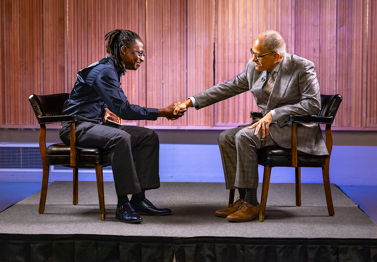 Student and Judge shake hands on a small stage with a bright wooden backdrop