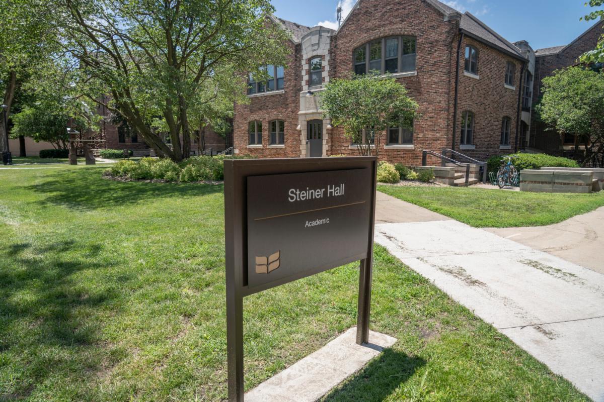 A brick building stands behind a green lawn and a sign reading Steiner Hall.