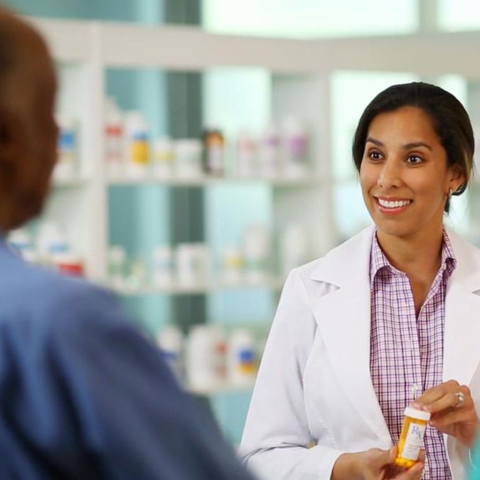 pharmacist holding pill bottle and talking to customer
