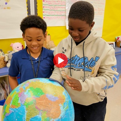 Two elementary school students in a classroom looking at a globe.