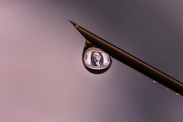 Dollar bill magnified in a drop of vaccine at the tip of a needle