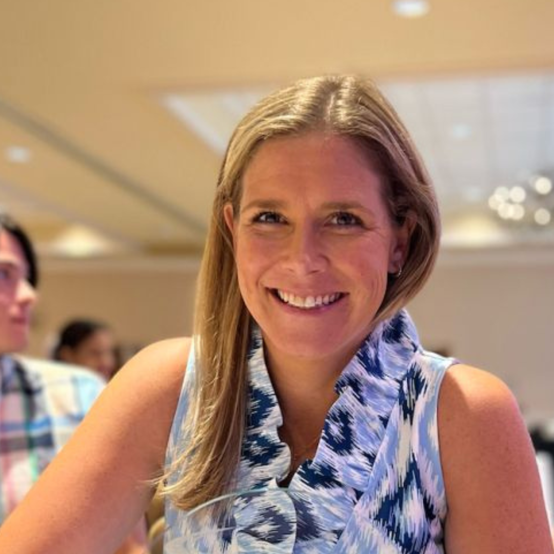 Young white woman smiling wearing a blue dress sitting in a conference room