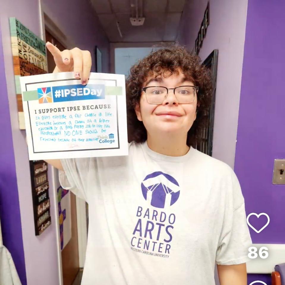 Young person with intellectual disability holding a handwritten sign with the IPSEDay logo that reads I support IPSE Day because it gives everyone a fair chance in life everyone deserves a chance  at a higher education or a good paying job to live life ind