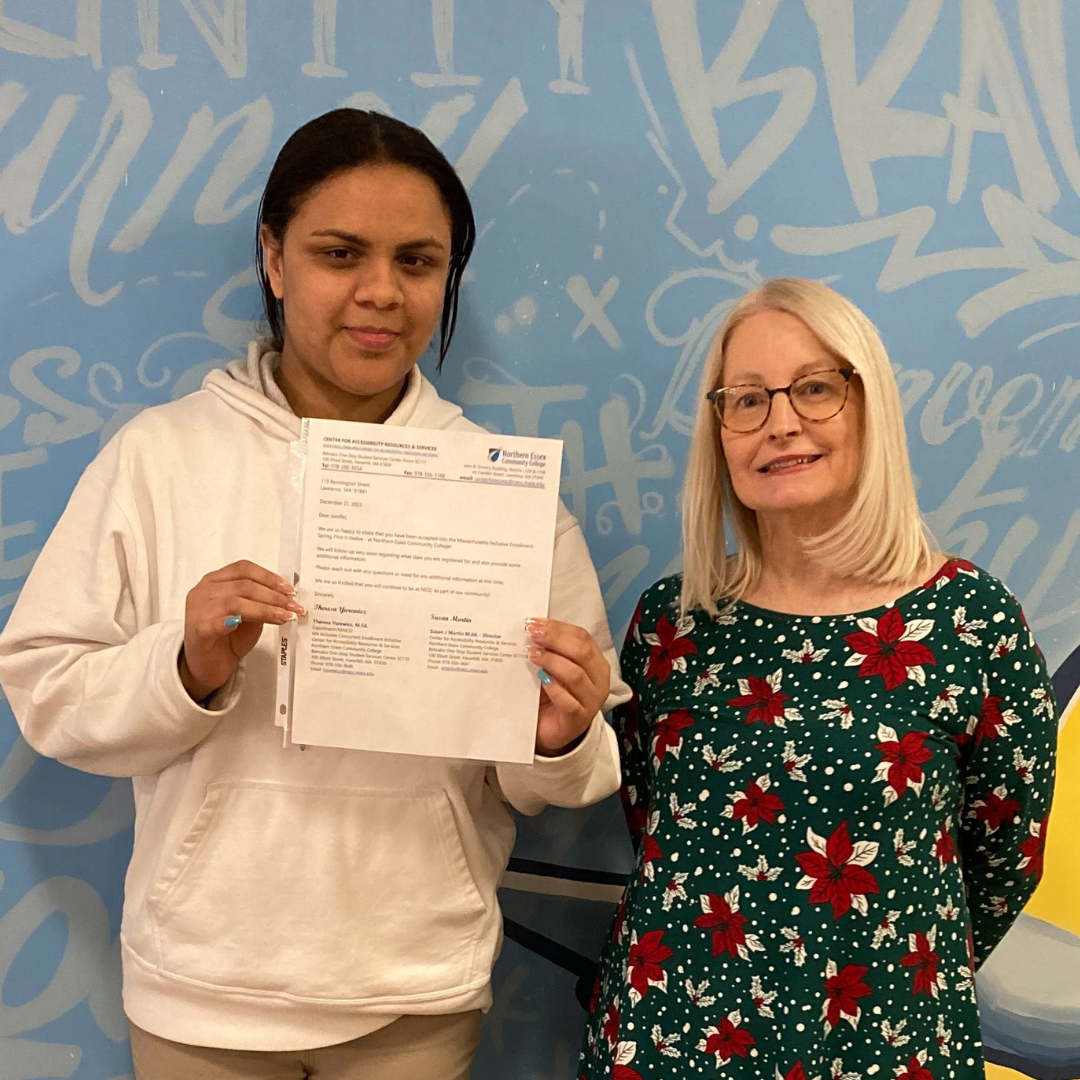 A student with a disability standing with an middle-aged woman and the student holds her acceptance letter document and she wears a white hoodie and beige pants, while the other wears glasses and a green dress with red flowers