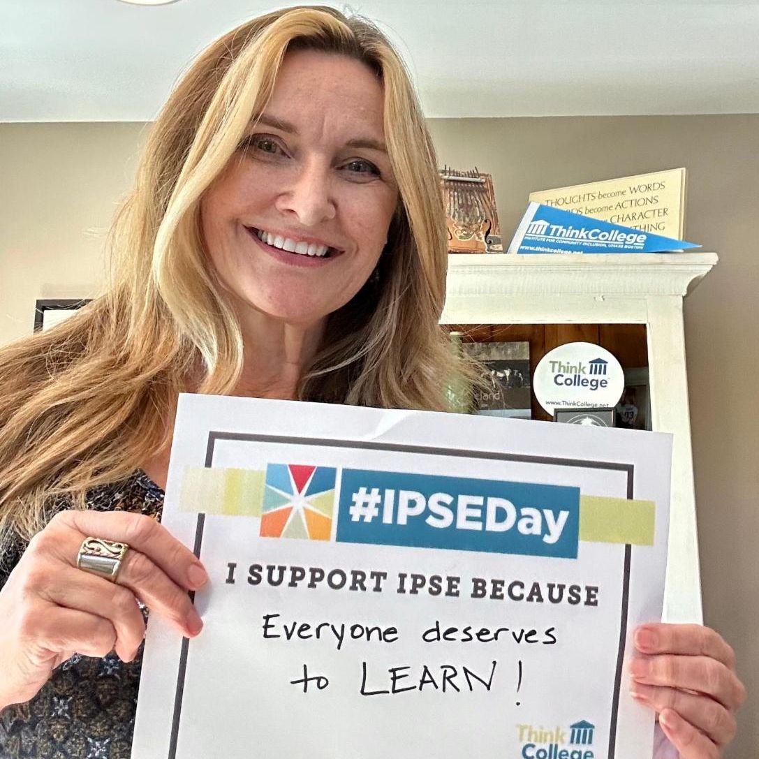 A woman standing indoors holding a sign that reads IPSEDay I support IPSE because everyone deserves to learn She is smiling and theres a Think College logo on the sign and a badge with the same logo in the background
