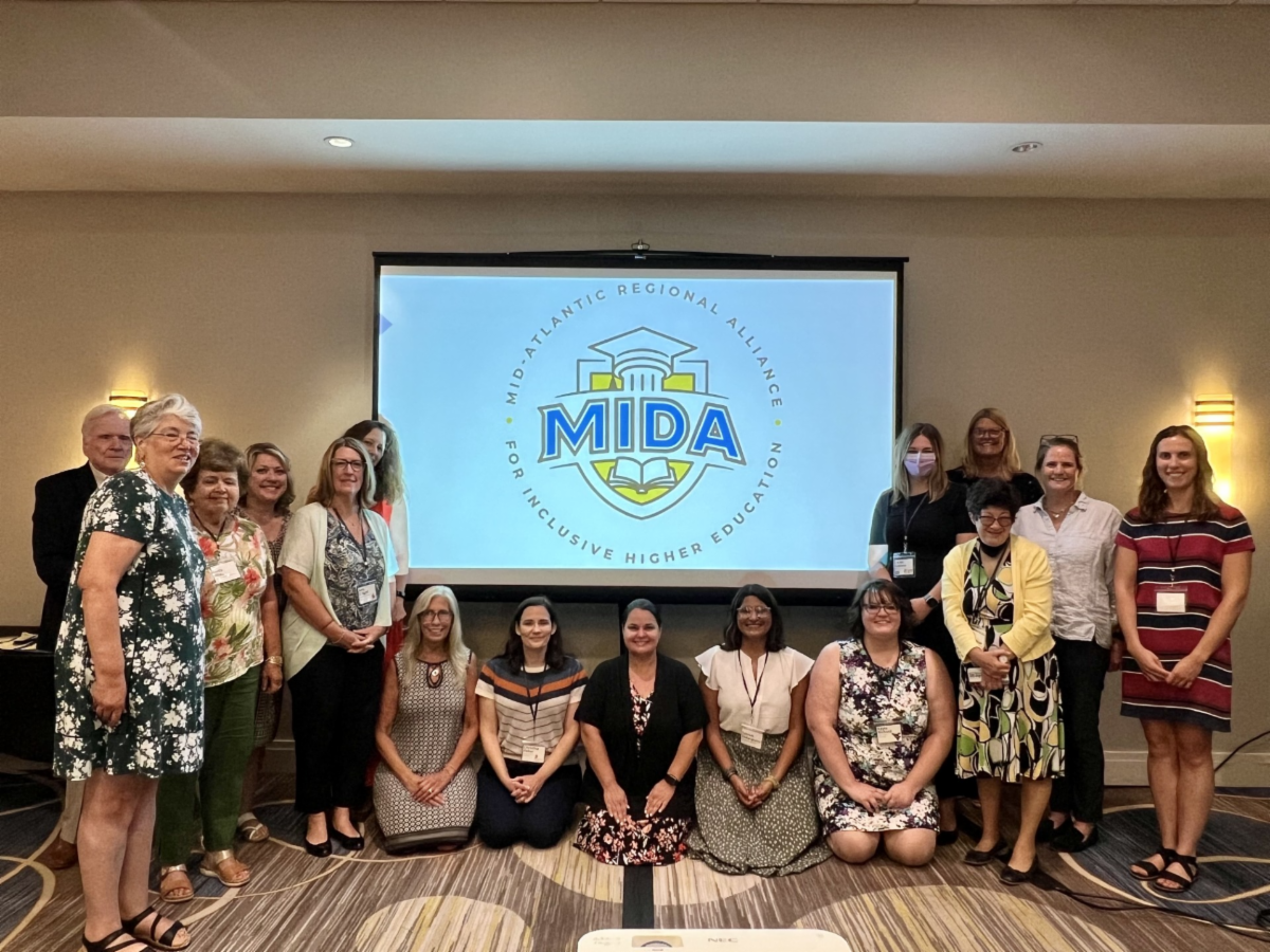 16 people standing in front of a screen with a PowerPoint slide with logo for MIDA