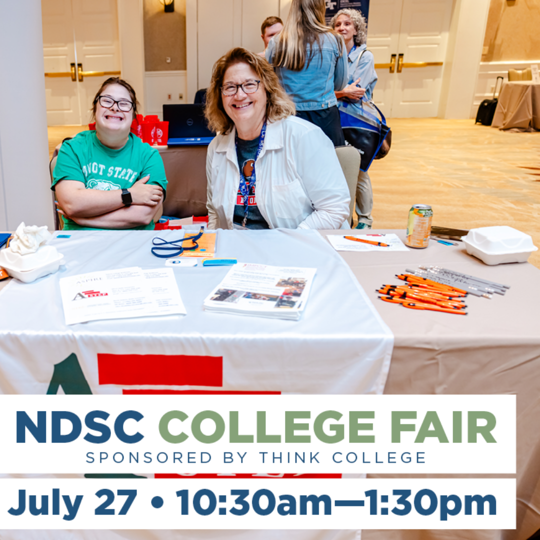 Two smiling women seated behind an exhibit table adorned with college swag