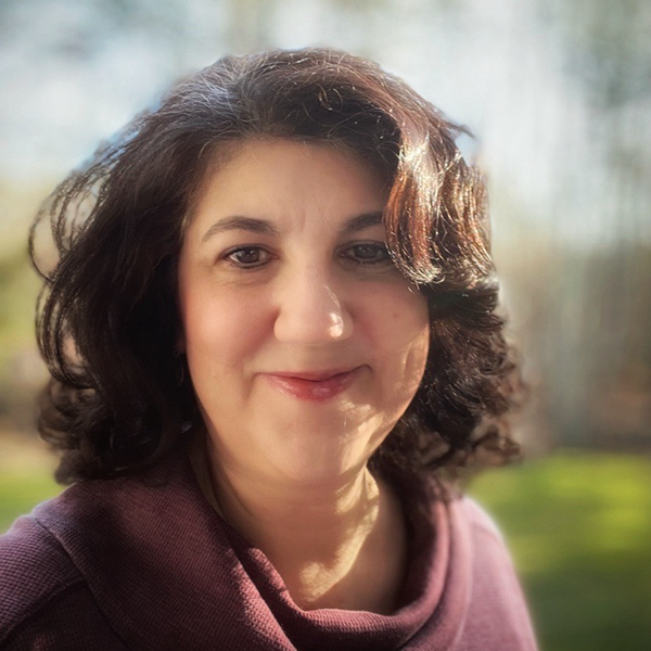 woman with dark hair wearing a purple sweater smiling with blurred outdoor background