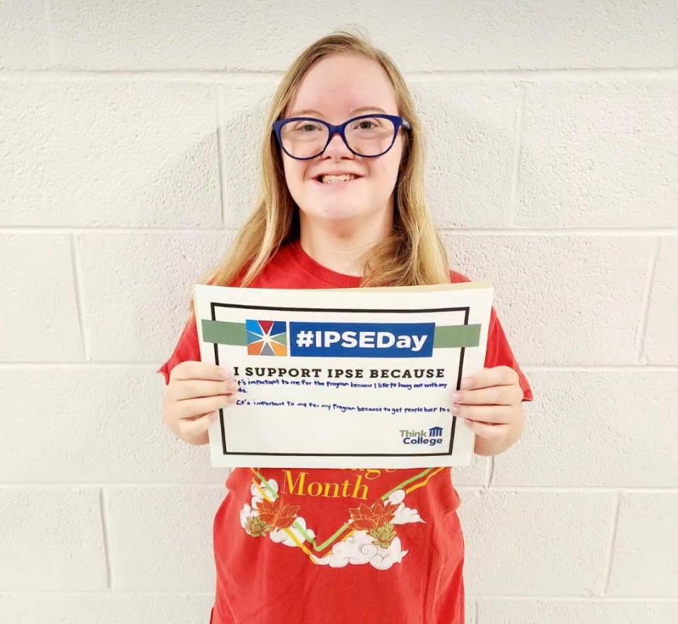 Young person with intellectual disability holding a handwritten sign with the IPSEDay logo that reads I support IPSE Day because it is important to me for the program because I like to handout out with my friends and it is important to me for the program b