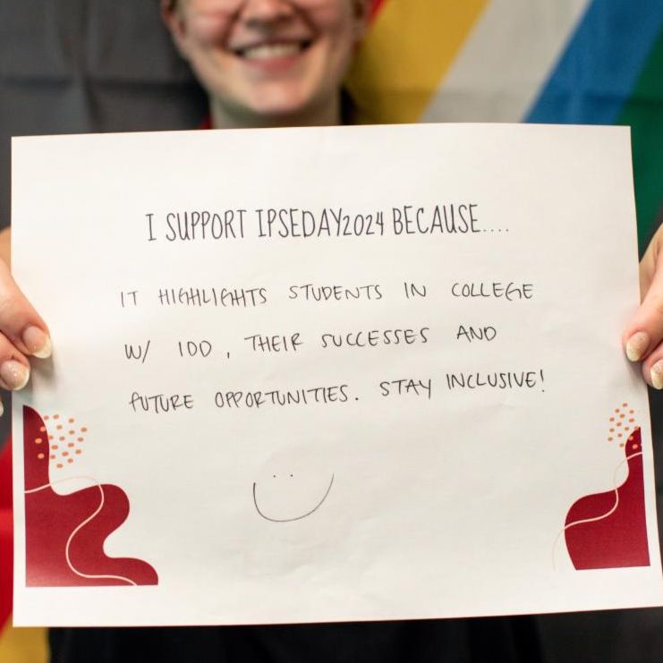 Person holding a sign over their face with the IPSE logo and the sign reads I support IPSE 2024 because it highlights students in college with IDD through successes and future opportunities stay inclusive with a smiley face
