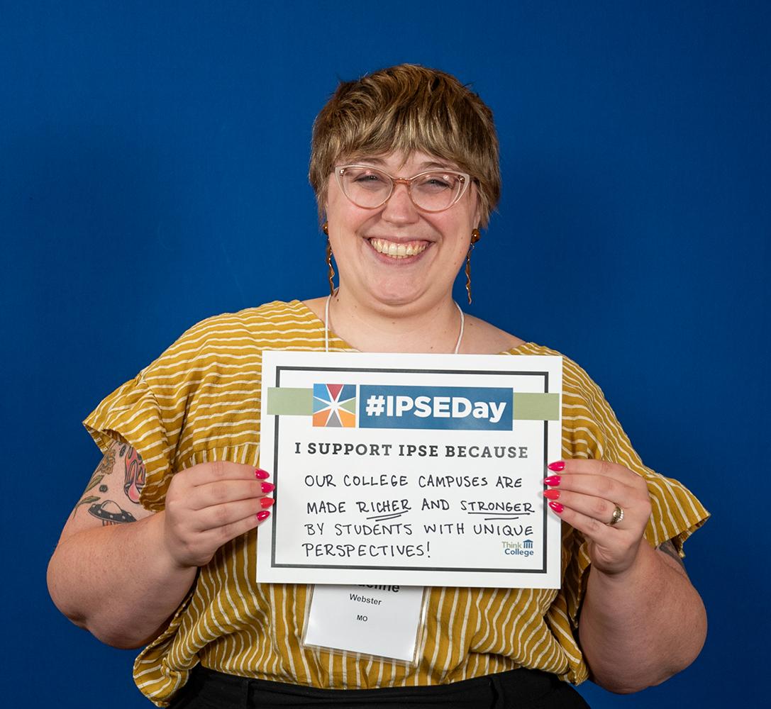 A person with short hair wearing glasses and a yellow striped shirt is smiling and holding a sign that reads I support IPSE because our college campuses are made richer and stronger by students with unique perspectives IPSEDay