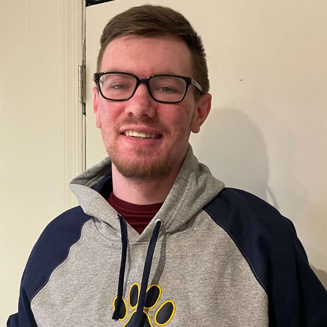 Young male student with eye glasses and a beard wearing a hoodie with a college mascot