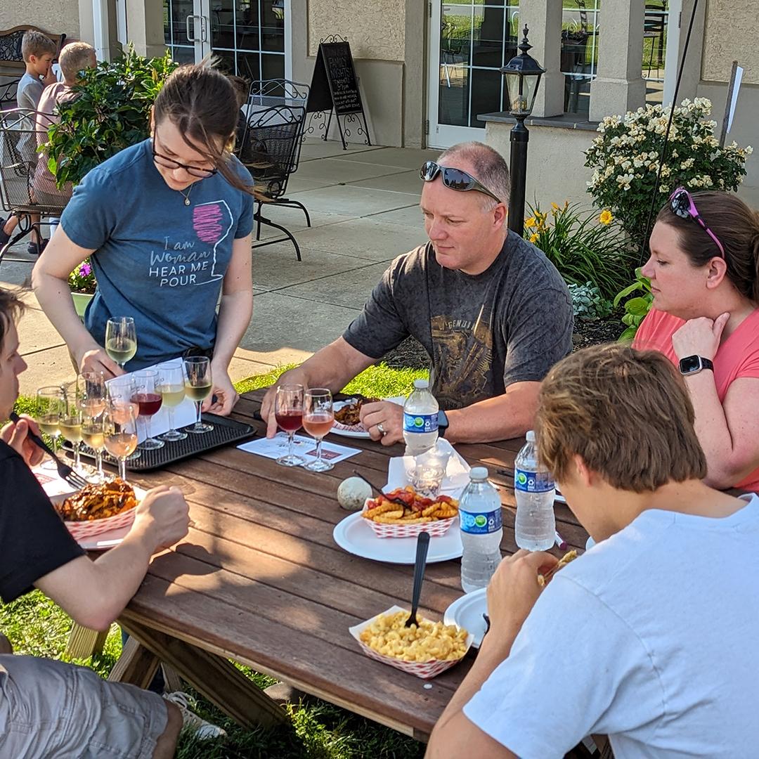 Family eating while adults wait for wine flights at Family Night