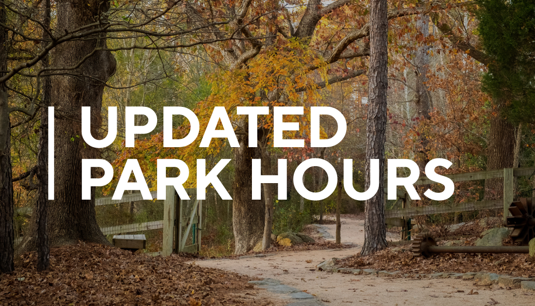 Text stating Updated Park Hours superimposed over image of pale dirt path curving around trees that have orange and red leaves.