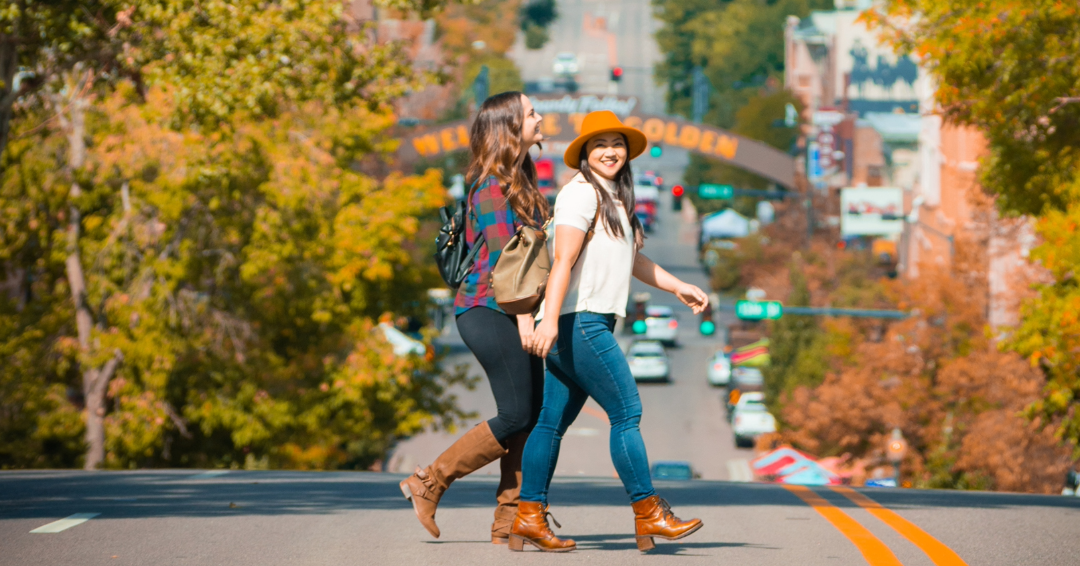 Two people cross a road smiling on a fall day