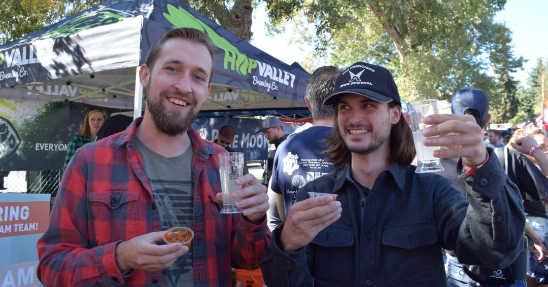 Two people hold up cups of chili at an outdoor festival