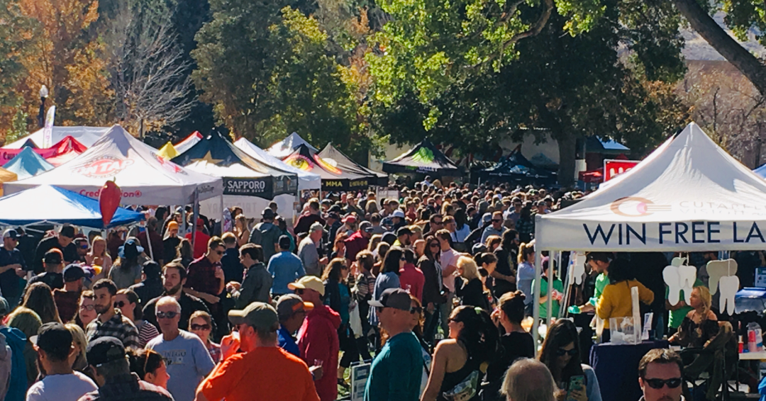 A large crowd at an outdoor festival with tents in the sunshine