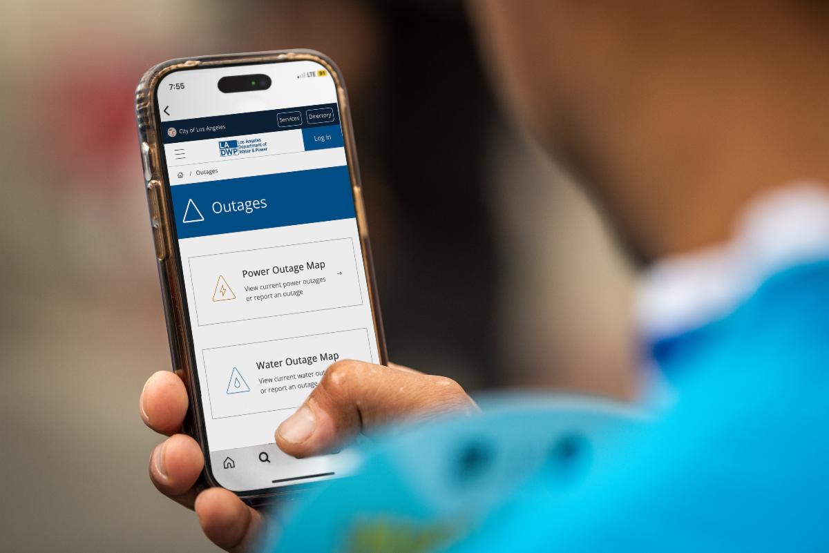 Person holding a mobile phone with the LADWP outages website on the screen.
