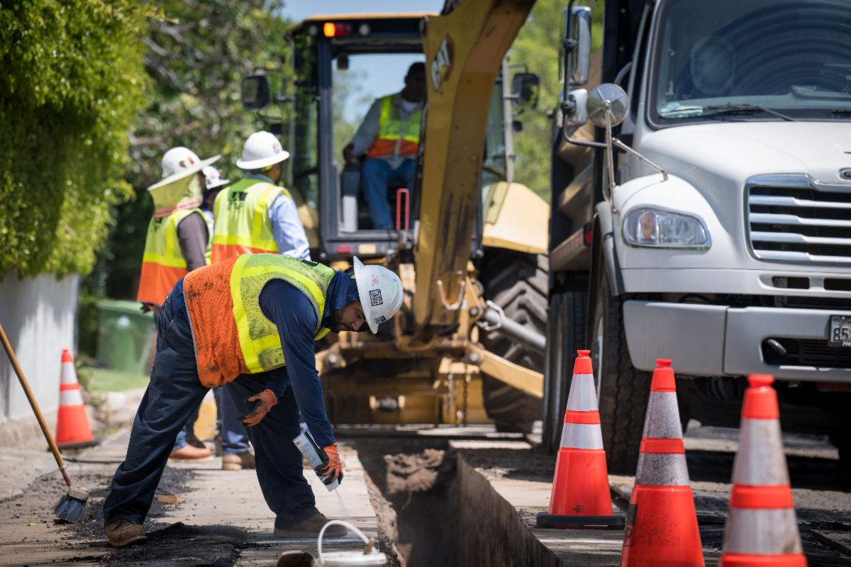 Construction crews working near open trench with bobcat and truck in the background