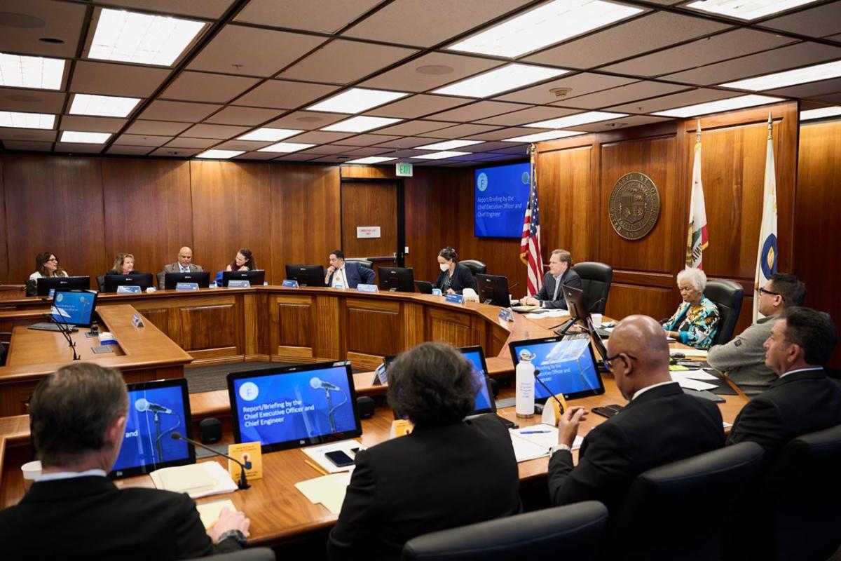  Group of people in board room sitting down with digital screens in front of them. 
