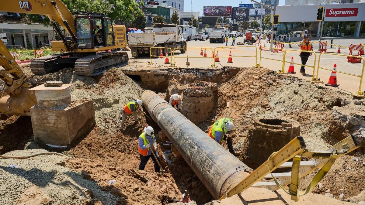 LADWP employees outdoors in safety vests working on water main line, with safety cones and vehicles in the background.