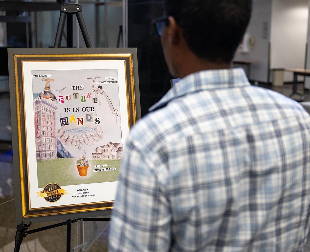 Man in checkered white blue and gray shirt looks at art poster on easel.