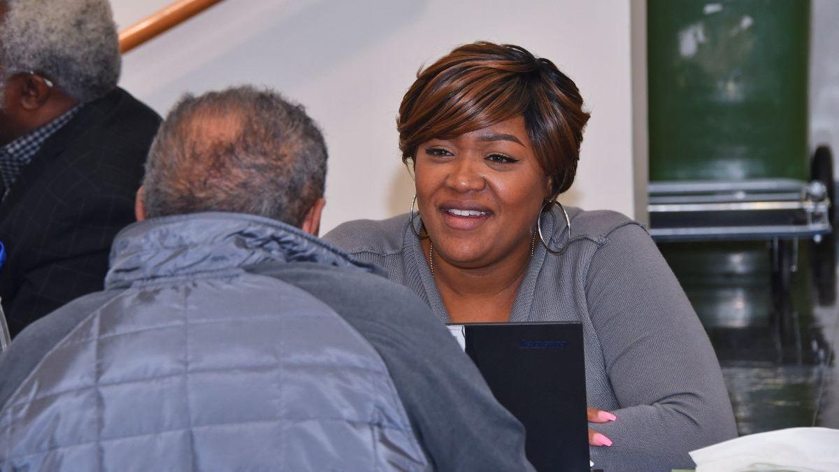 Smiling woman seated behind a desk talking to a person facing her.