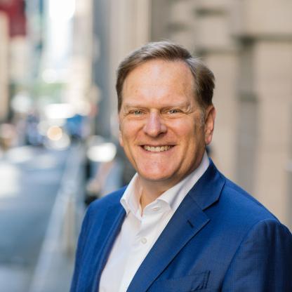 Smiling man is outdoors in a blue suit with white undershirt.