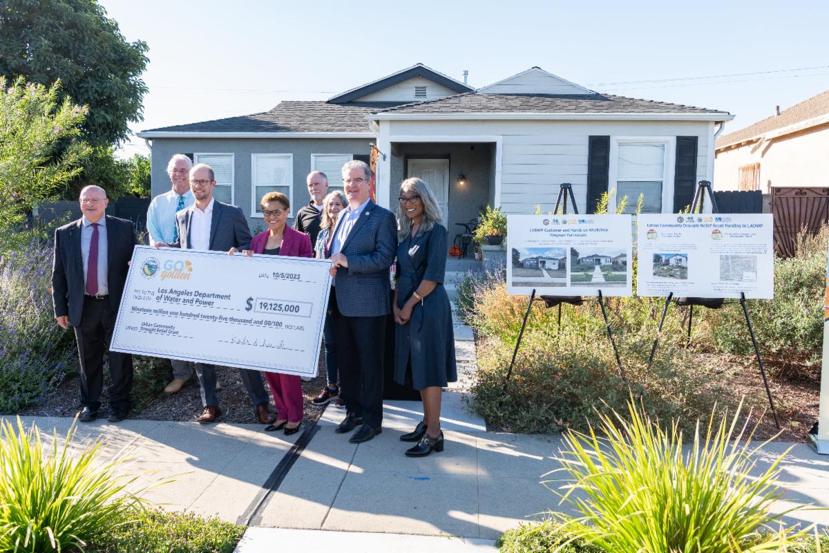 Group of state and city leaders gathered around holding a prop check in front of a customer's home to announce grant funding received