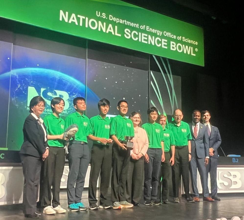 Group of students in green polo starts standing on a stage. 