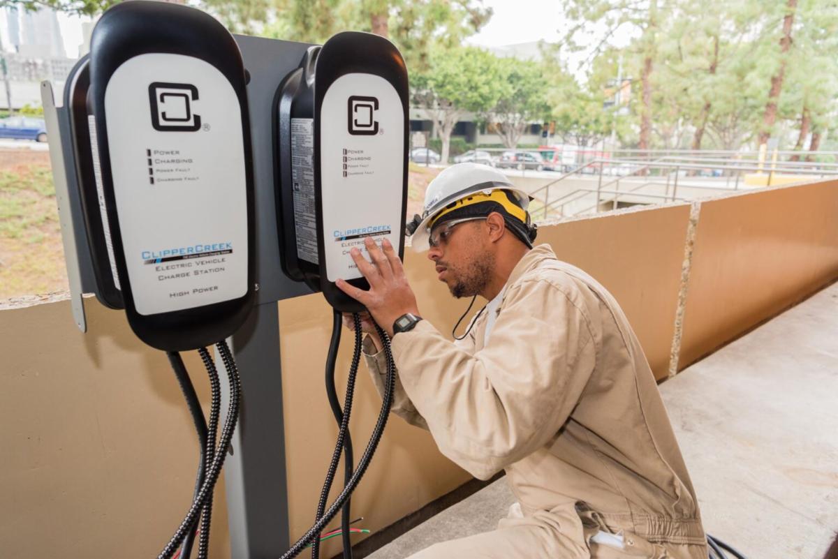 Male employee kneeling and working on an outdoor EV charger unit. 