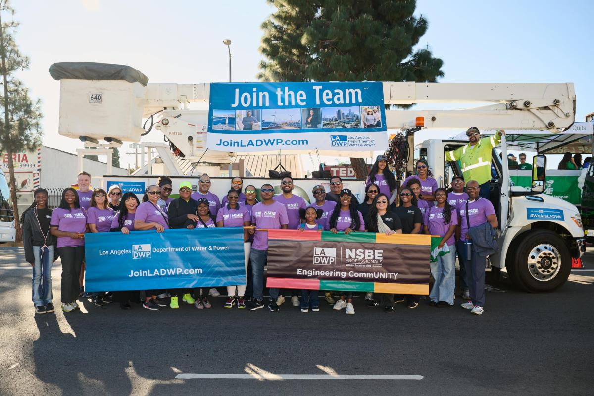  Group of people posing for a picture outdoors on a street in front of an LADWP bucket truck with a banner that reads, “Join the Team. JoinLADWP.com.”
