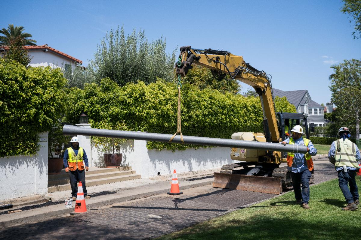 3 LADWP construction crew members holding a pipe, using a bobcat to lower it into the ground