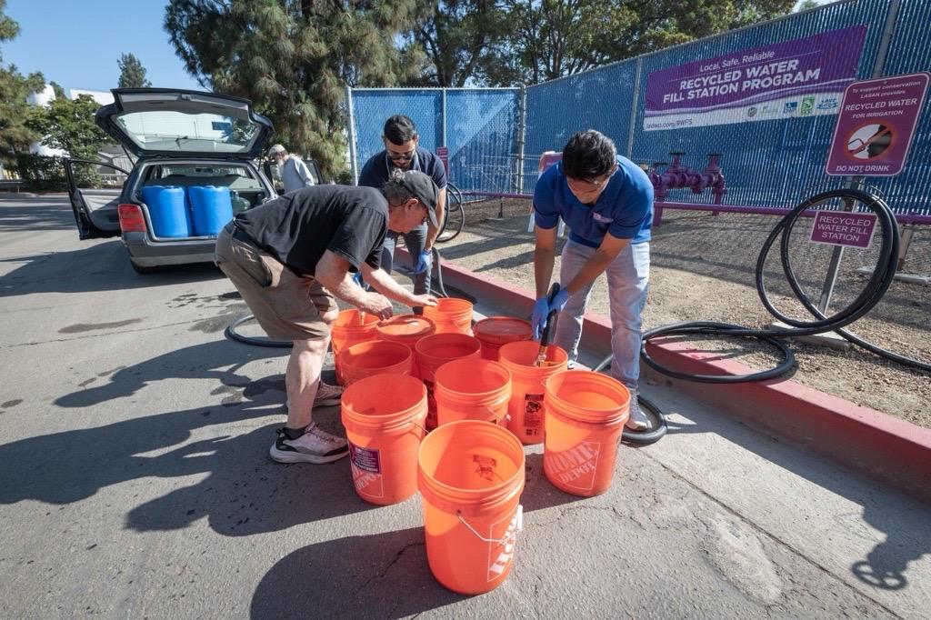 Three men outside filling up orange buckets with recycled water. 