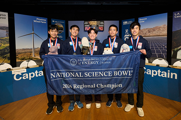 Five male students on stage wearing medals and holding a “2026 Regional Champion” banner.