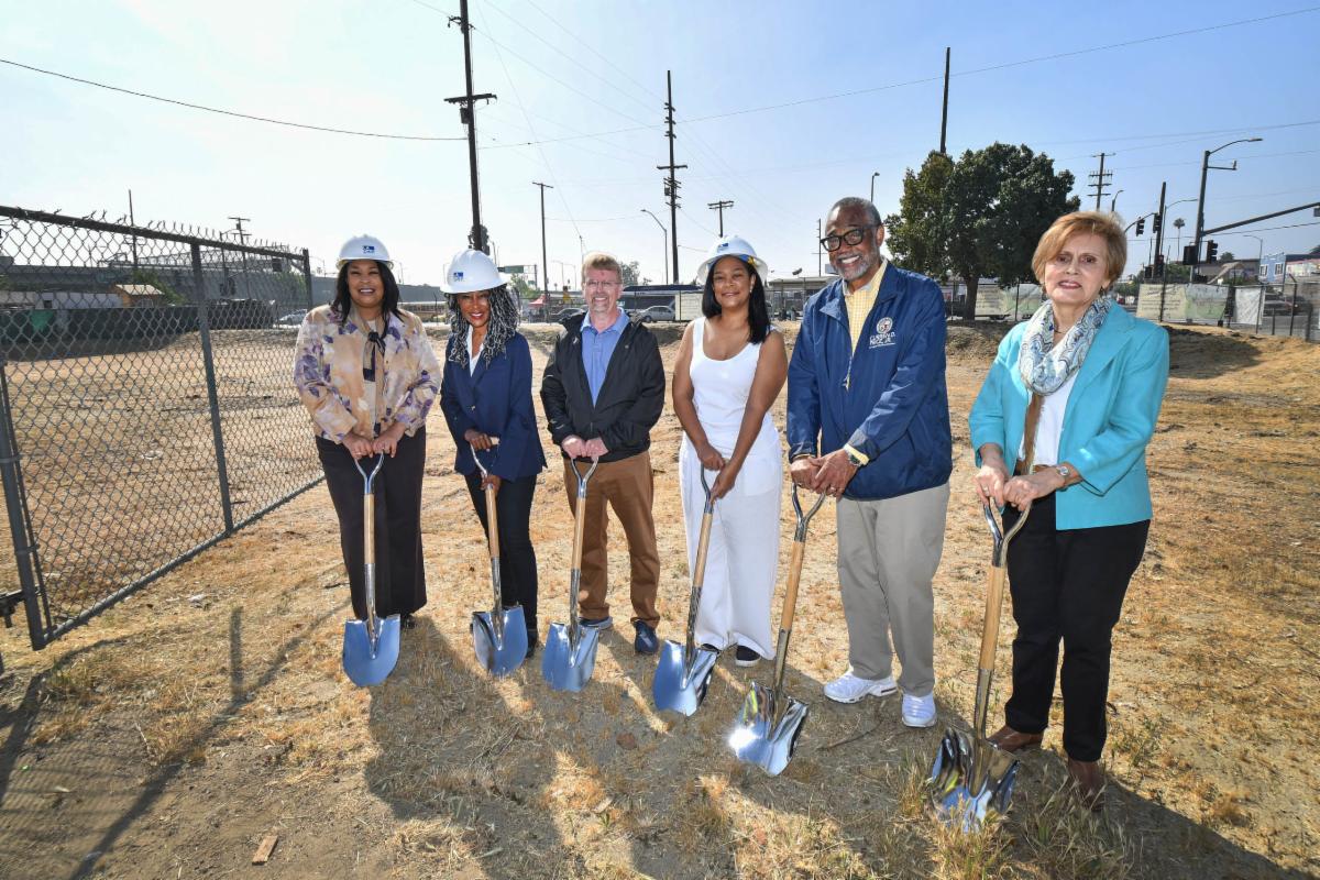 Image of a group of people standing on dirt holding shovels smiling for the camera