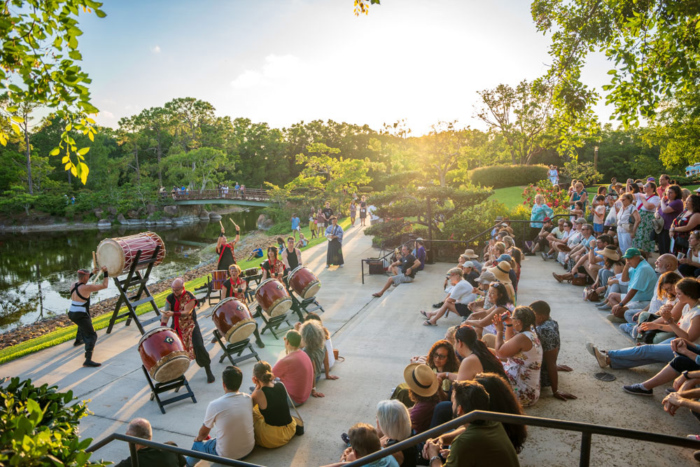 Image of a group of people watching a drum performance in the afternoon near a lake