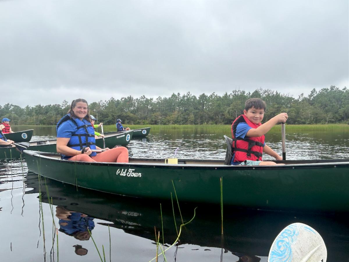 Image of 2 people canoeing on a green canoe on a lake