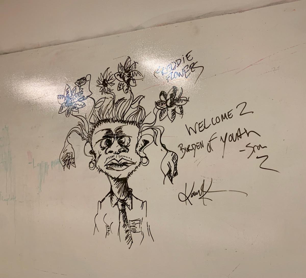 an illustrated image created on a whiteboard with a black dry erase marker. the image resembles a masculine-presenting character with flowers for hair. the character's face is expressionless and they're wearing a button up with a tie and hoop earrings.
