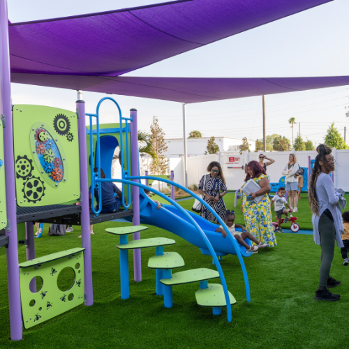 Children and families enjoying an inclusive playground with slides and shade structures at the New Children Services Center