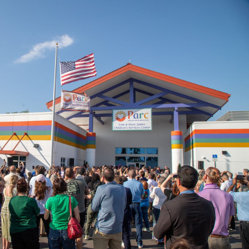 Crowd gathered outside Parc Center for Disabilities building during a grand opening event with an American flag overhead