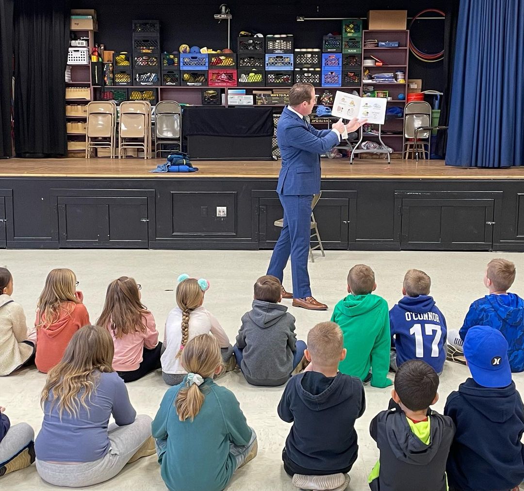 Middletown Township Mayor Tony Perry stands in front of a group of seated Lincroft Elementary School students and leads the class' daily read aloud.