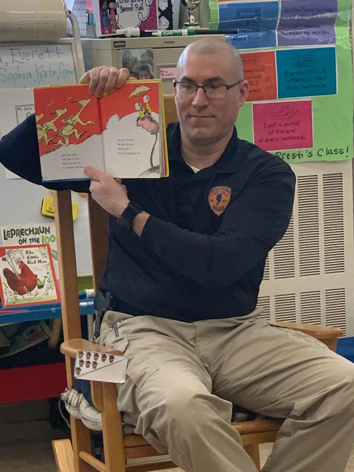 A male officer of the Middletown Township Police Department holds up a Dr. Seuss book while reading to Lincroft Elementary School students.