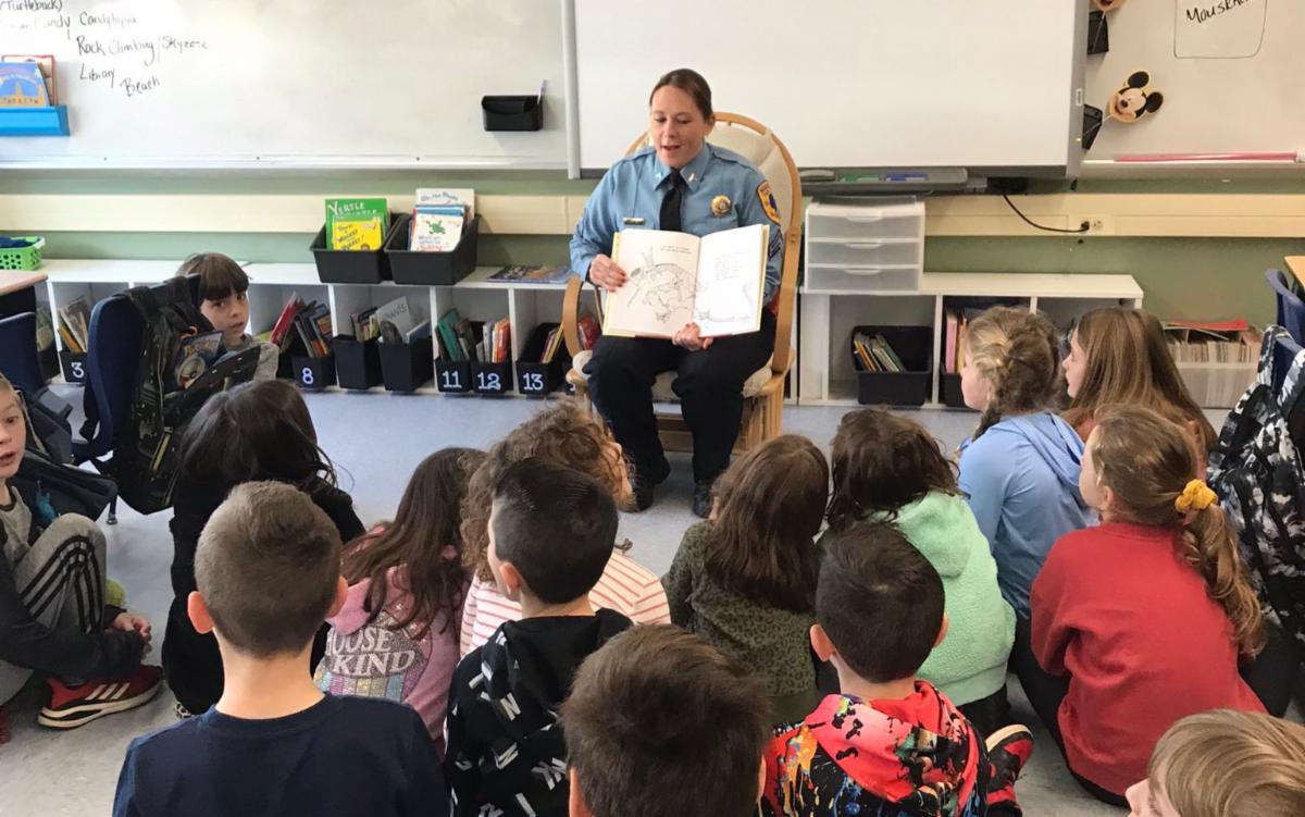A female officer of the Middletown Township Police Department is encircled by, and reading too, Lincroft Elementary School students.