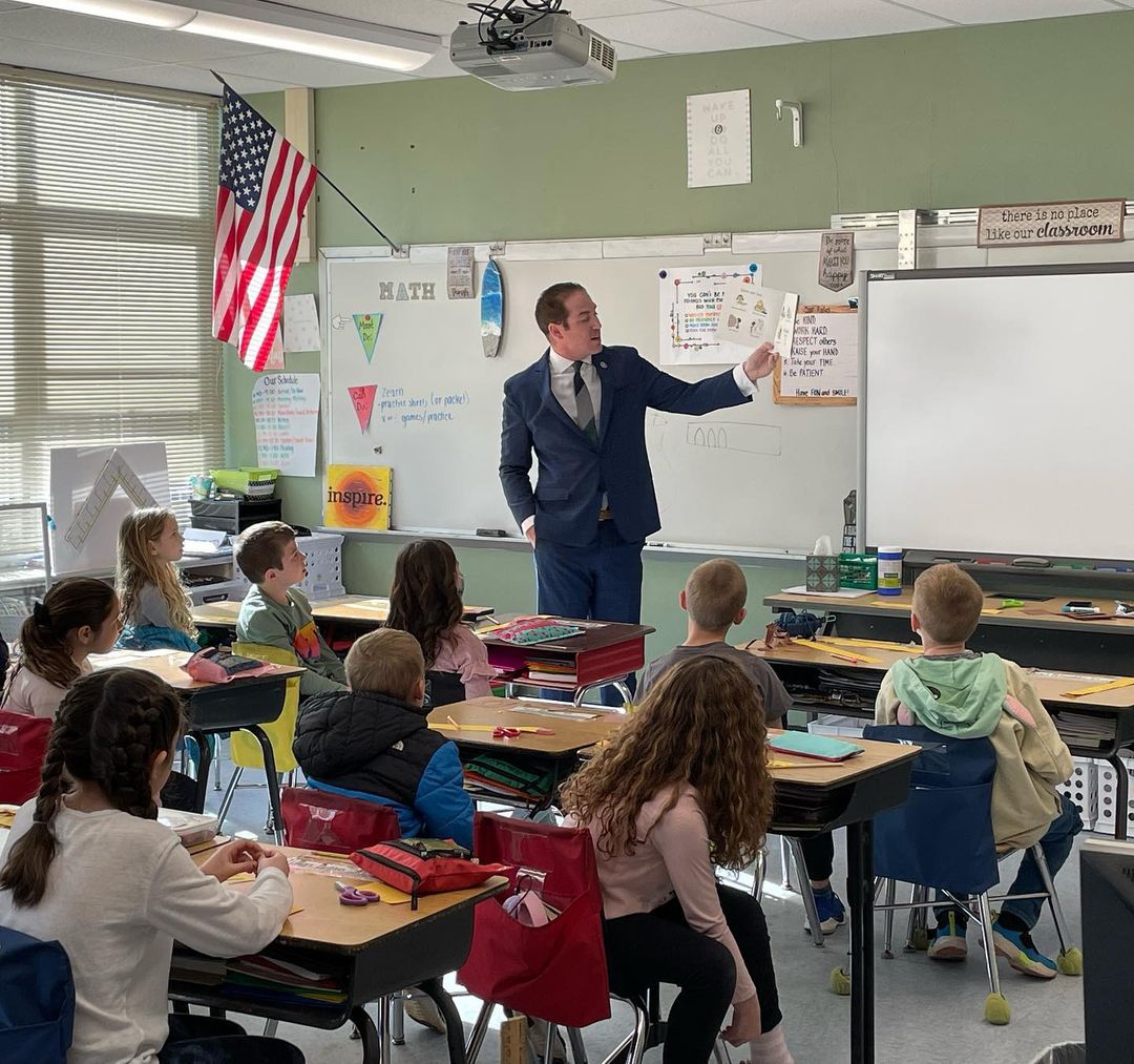 Middletown Township Mayor, Tony Perry, stands at the front of the Lincroft Elementary School classroom and reads a book to a group of students.