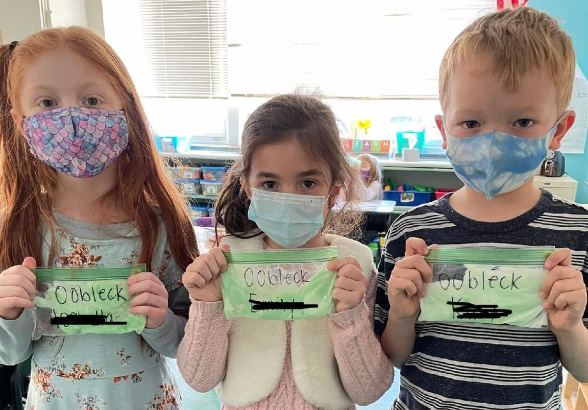 Three elementary school children hold bags of green Oobleck.